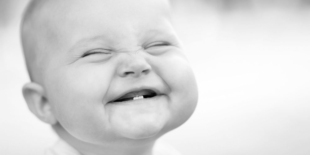 Zahnarzt Erlangen – lachendes Baby mit erstem Zahn als Symbolbild für Zahngesundheit bei zhochdrei